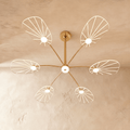 Clérachic leaf-shaped chandelier with 6 lit acrylic panels radiating from a brass stem, glowing warm on a plaster ceiling.