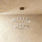 Clérachic two-tier round chandelier with opal spherical shades on a dark bronze-toned frame, lit, against limewashed plaster.