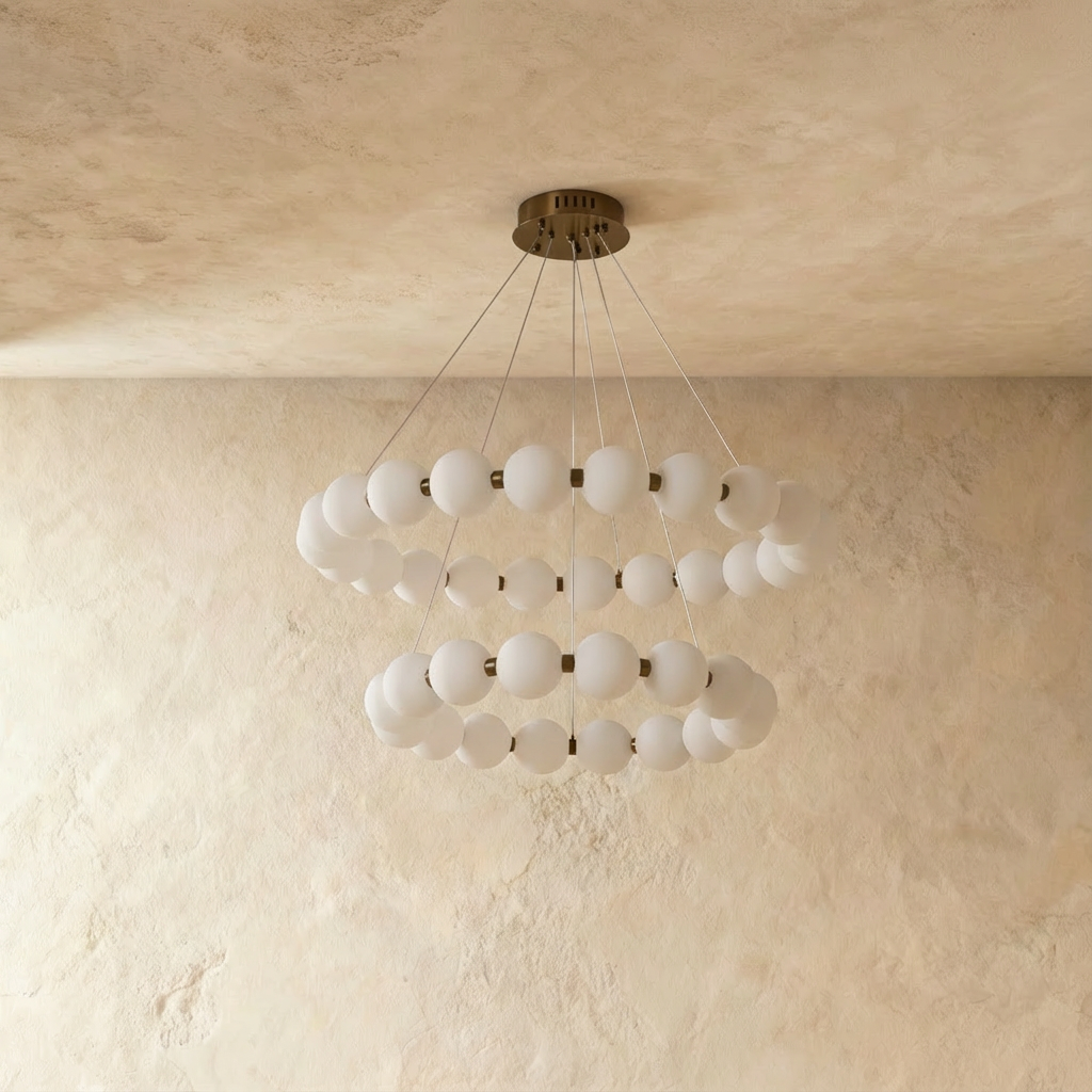 Clérachic two-tier round chandelier with opal spherical shades on a dark bronze-toned frame, lit, against limewashed plaster.
