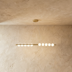 Clérachic linear chandelier in gold finish, a long oval rail holding ten opal spherical shades, suspended on fine wires.