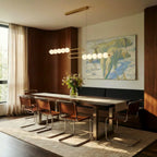 Clérachic S-shaped linear chandelier with opal globes hanging over a long dark dining table and leather cantilever chairs.