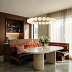 Clérachic one-tier round chandelier of opal spherical shades above a terrazzo oval table and a banquette in a dining nook.