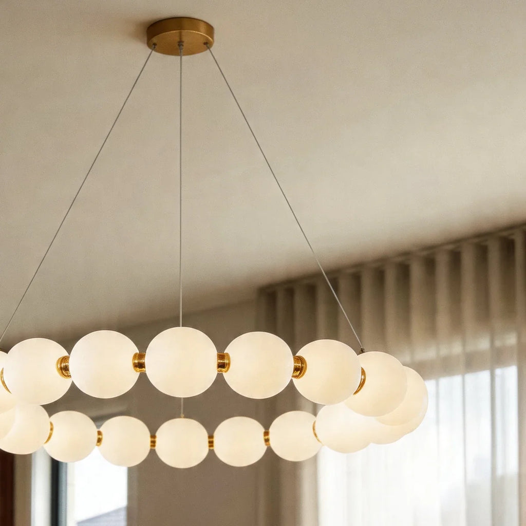 Close view of the Clérachic one-tier round chandelier, lit opal spheres joined by gold-finished collars on thin suspension wires.