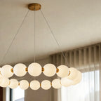 Close view of the Clérachic one-tier round chandelier, lit opal spheres joined by gold-finished collars on thin suspension wires.