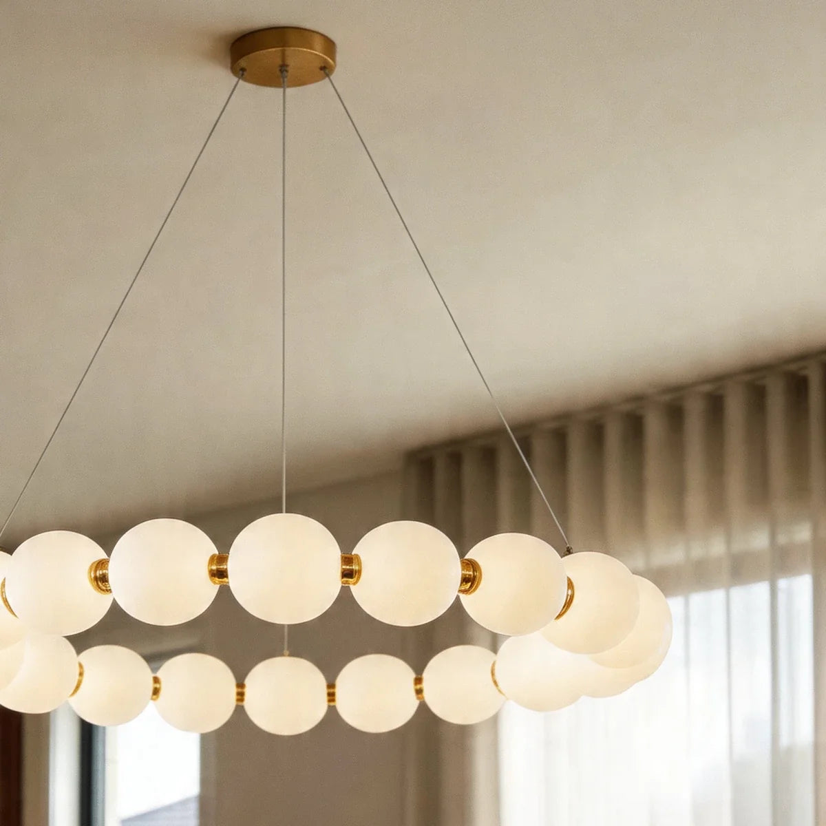 Close view of the Clérachic one-tier round chandelier, lit opal spheres joined by gold-finished collars on thin suspension wires.