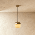 Clérachic alabaster pendant light, a single glowing stone drum shade under a brass dome, hung from a plaster ceiling.