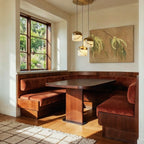 Three Clérachic alabaster pendant lights glow warm above a walnut banquette, beside a window and framed botanical art.
