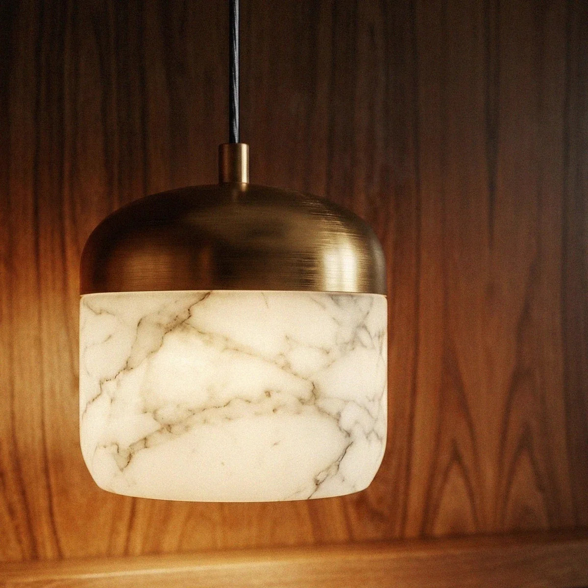 Close-up of a Clérachic alabaster pendant light, its veined stone shade glowing warm under a brushed brass dome.