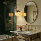 Two Clérachic alabaster pendant lights glow warm beside a green-tiled shower and an oval mirror in a bathroom.