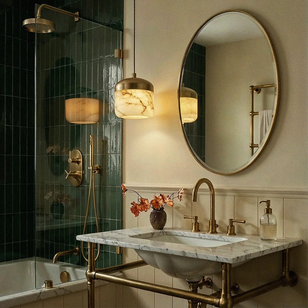 Two Clérachic alabaster pendant lights glow warm beside a green-tiled shower and an oval mirror in a bathroom.