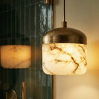 Close-up of a Clérachic alabaster pendant light glowing warm beside a mirror reflecting a second fixture nearby.