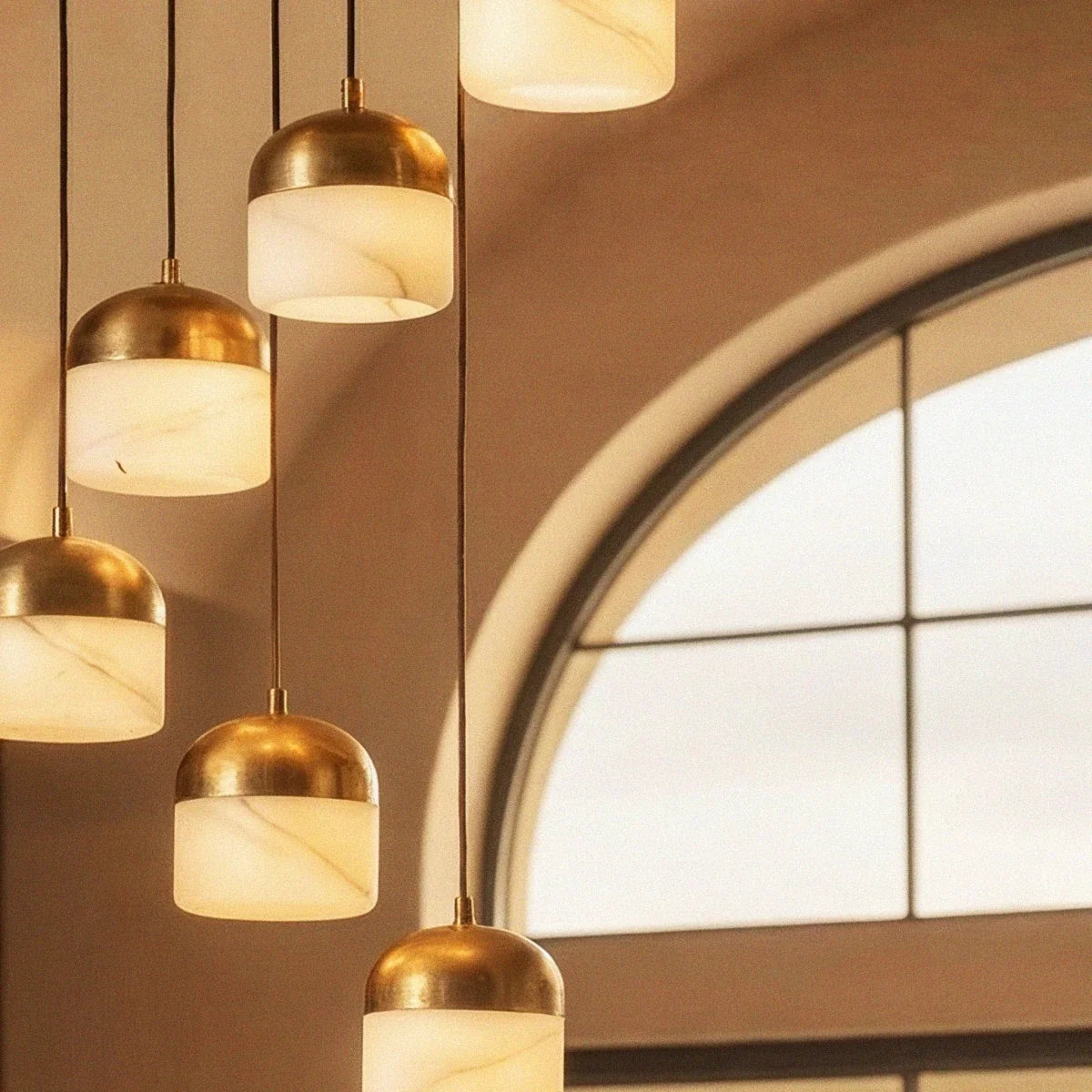 Close-up of the Clérachic alabaster pendant cluster, several stone shades glowing warm beside an arched window.