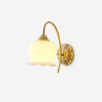 Brass wall light from Clérachic with a cream glass shade shaped like a bell flower on a curved arm, on a plain white backdrop.