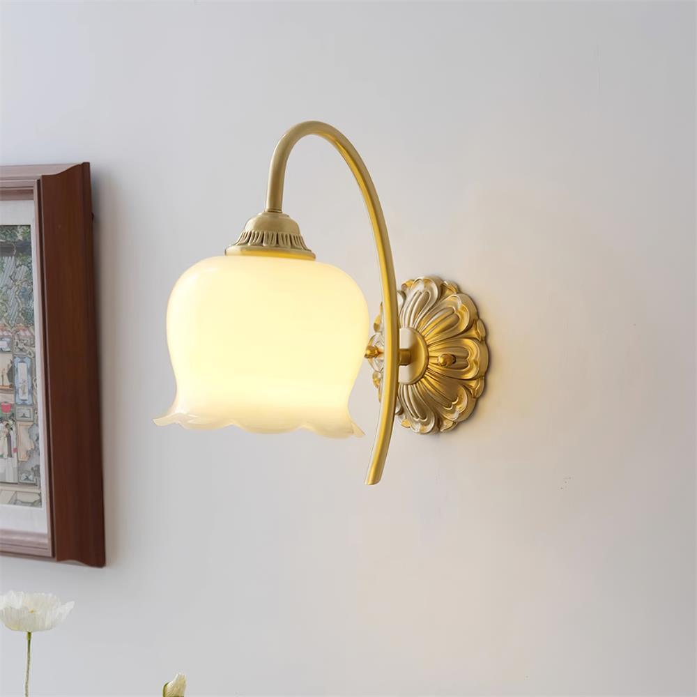 Lit Clérachic wall light with a scalloped cream glass shade and a brass arm, beside a framed picture on a pale wall.