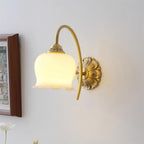 Lit Clérachic wall light with a scalloped cream glass shade and a brass arm, beside a framed picture on a pale wall.