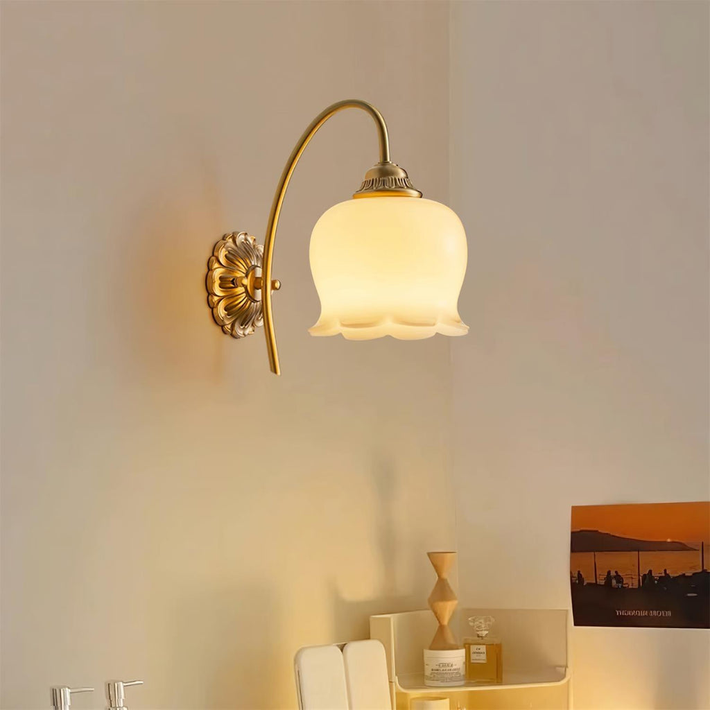 Clérachic brass wall light with a warm-glowing flower-shaped shade above a shelf of small decor and a sunset print.