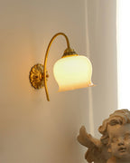 Lit Clérachic wall light with a bell-shaped glass shade beside a pale curtain and a cherub figure in the corner.