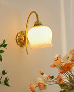 Clérachic brass wall light lit beside a bunch of orange and white poppies against a warm beige wall.