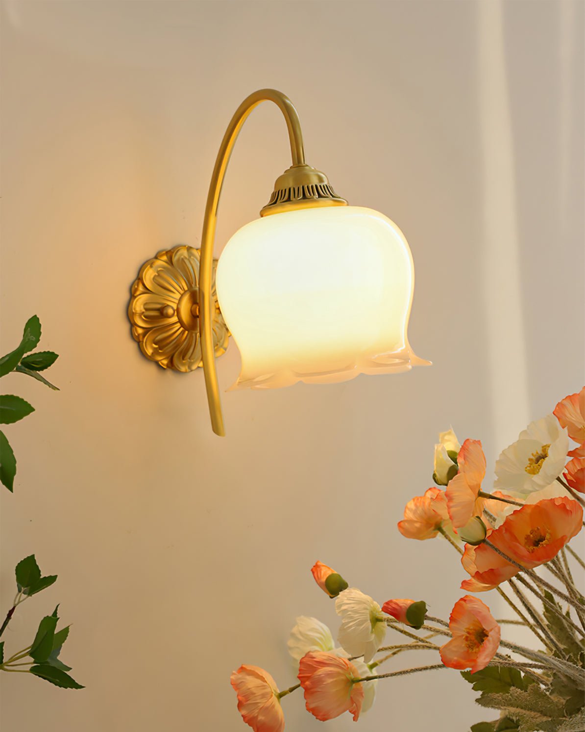 Clérachic brass wall light lit beside a bunch of orange and white poppies against a warm beige wall.