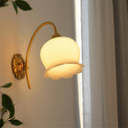 Angled view from below of the Clérachic wall light lit, showing the frilled rim of the glass shade and the brass back plate.