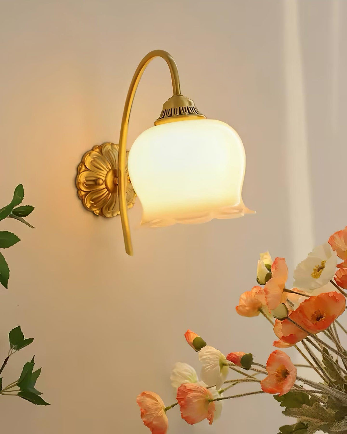 Clérachic wall light glowing warm beside a vase of poppies, its brass arm and flower-shaped shade clear on a beige wall.