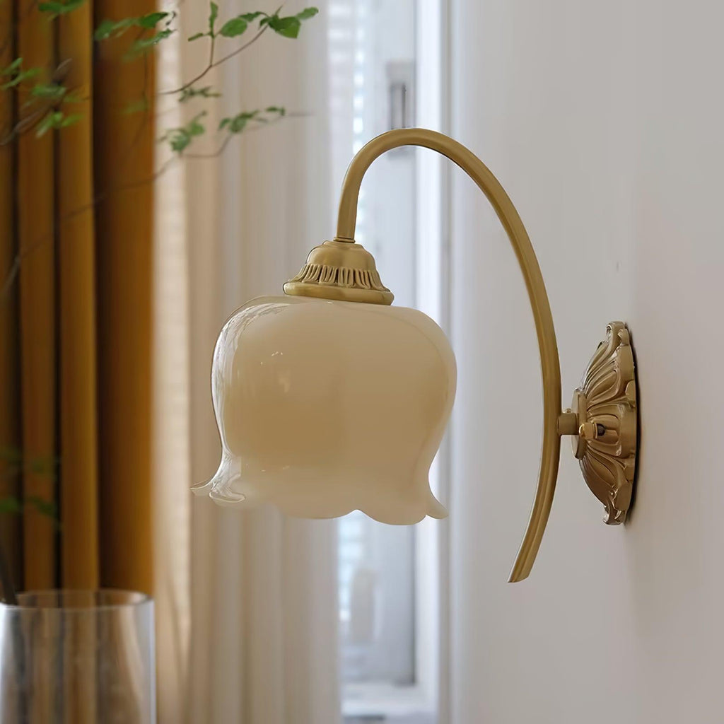 Cream glass flower shade on a brass arm, a Clérachic wall light beside gold curtains and a window.