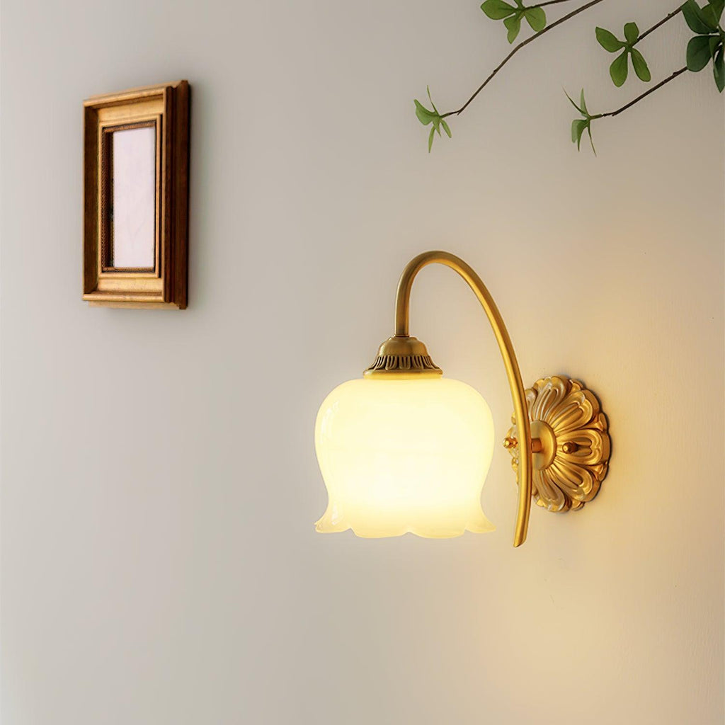 Lit Clérachic wall light beneath a small wooden frame and a leafy twig, its glass shade glowing a soft white.