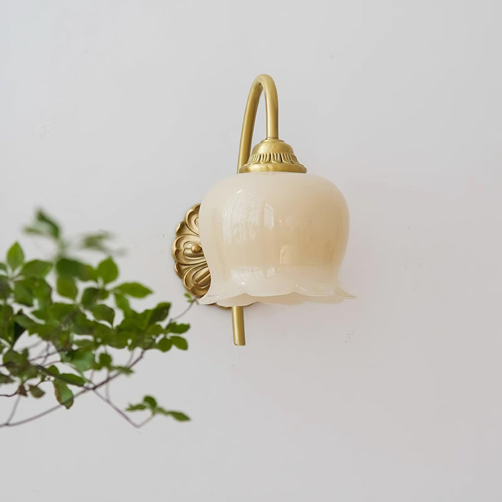 Clérachic wall light with a cream glass bell shade, set partly behind green leaves on a white wall.