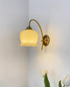 Clérachic brass wall light glowing warm in a room corner, with tulips in the foreground.