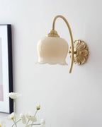 Unlit Clérachic wall light with a cream glass shade, next to a black-framed picture and a spray of white flowers.