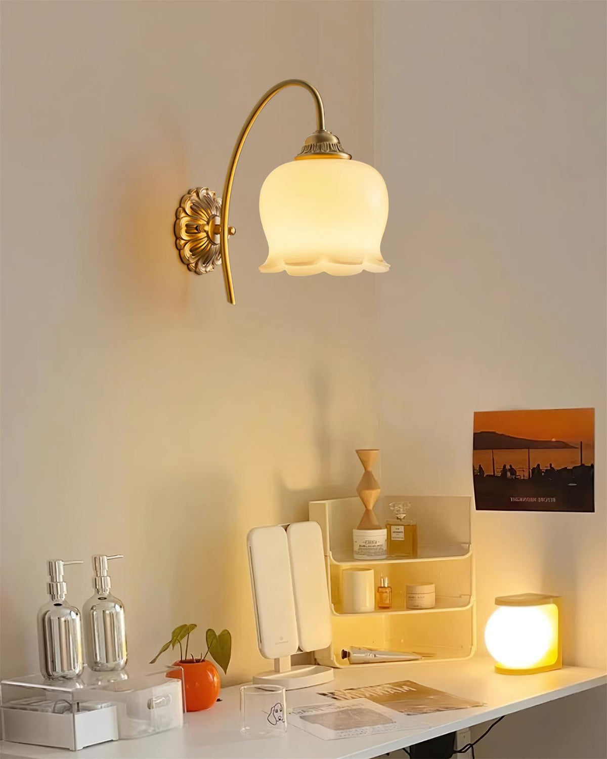 Clérachic brass wall light glowing above a white desk with a vanity mirror, skincare bottles and a small lamp.
