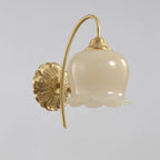 Clérachic brass wall light with a frilled cream glass shade and ornate round back plate, on a plain grey background.