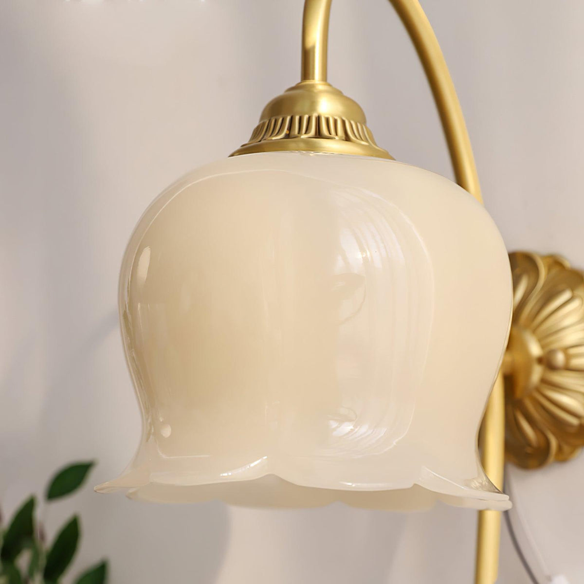 Close view of the cream glass bell and the ridged brass cap where it meets the arm on this Clérachic wall light.