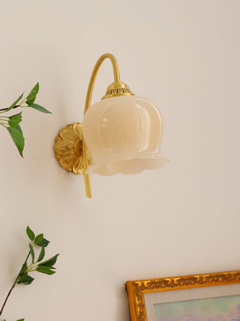 Unlit Clérachic wall light with a cream glass shade, beside green leaves and a gold-framed painting.
