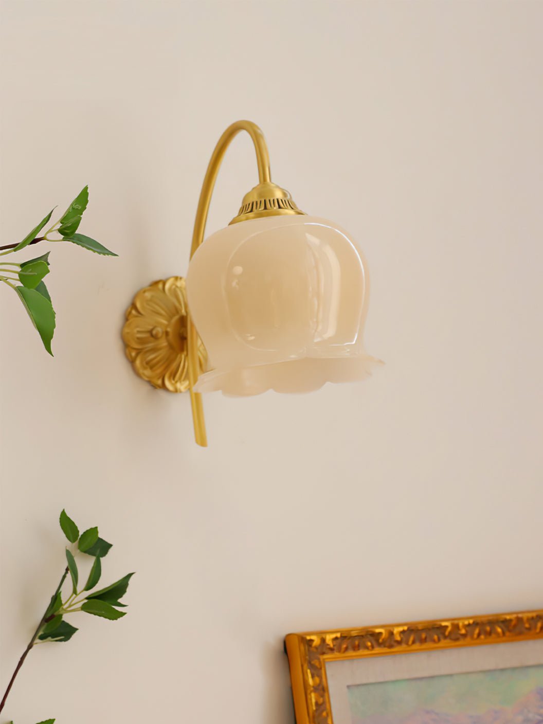 Unlit Clérachic wall light with a cream glass shade, beside green leaves and a gold-framed painting.