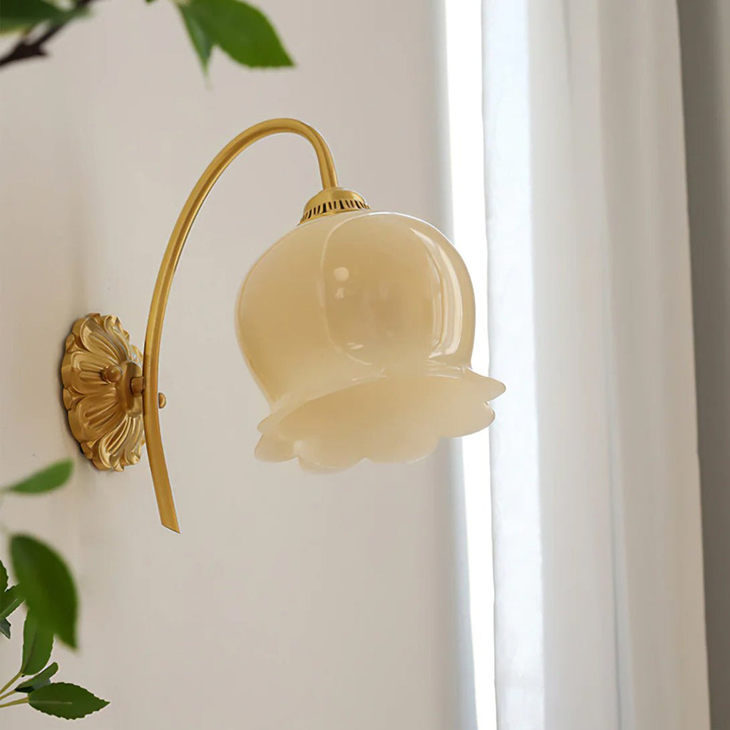 Angled view of the Clérachic wall light with a ribbed cream glass shade, beside a white curtain and green leaves.