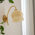 Angled view of the Clérachic wall light with a ribbed cream glass shade, beside a white curtain and green leaves.