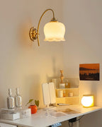 Clérachic brass wall light lit above a desk with a vanity mirror, a small lamp and a sunset poster.