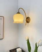 Clérachic wall light lit in a white room corner, above a vase of white tulips and a framed print.