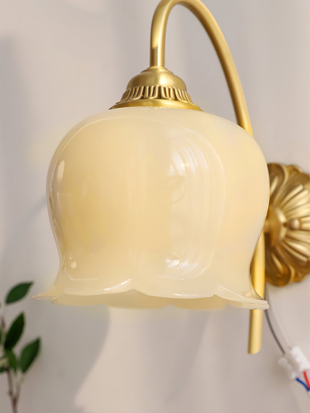 Close view of the ribbed cream glass shade and brass cap on this Clérachic wall light, with the cable showing at the back.