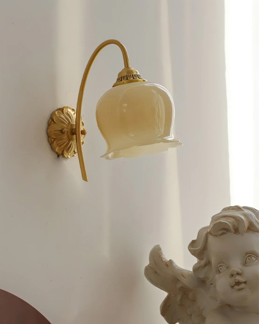 Clérachic wall light with a cream glass bell shade against a white curtain, with a cherub figure at the lower right.