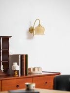 Unlit Clérachic wall light with a cream glass shade above a wooden chest, a row of books and a small candle holder.