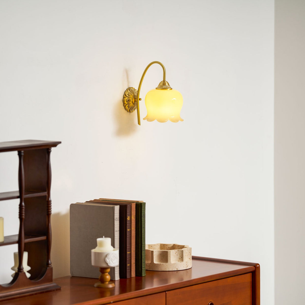 Lit Clérachic wall light glowing warm over a wooden chest with books and a travertine-look tray.