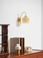 Unlit cream glass shade on a Clérachic wall light, above a wooden shelf unit, books and a candle.
