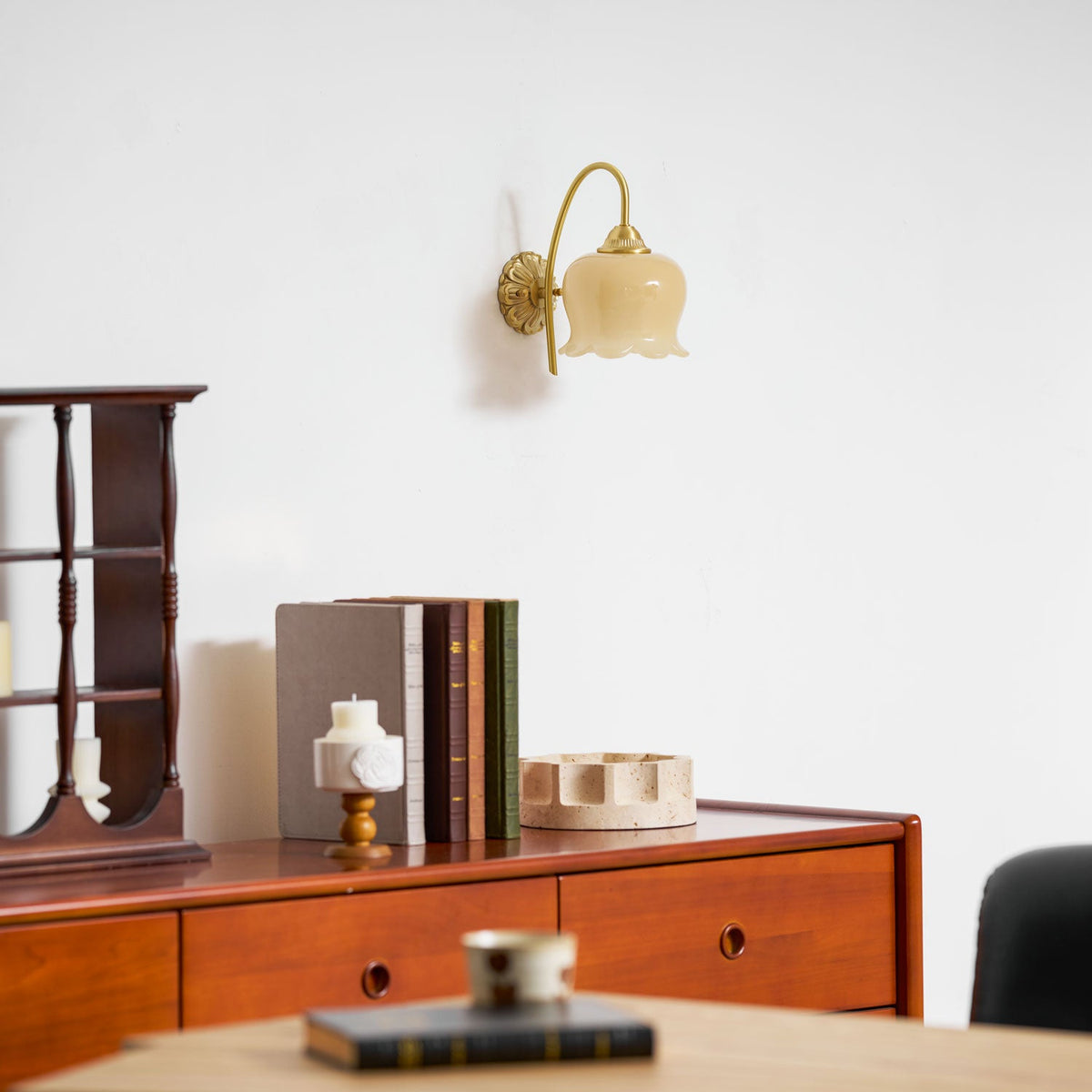 Unlit Clérachic wall light above a wooden chest with books, a stone tray and a table with a cup in the foreground.