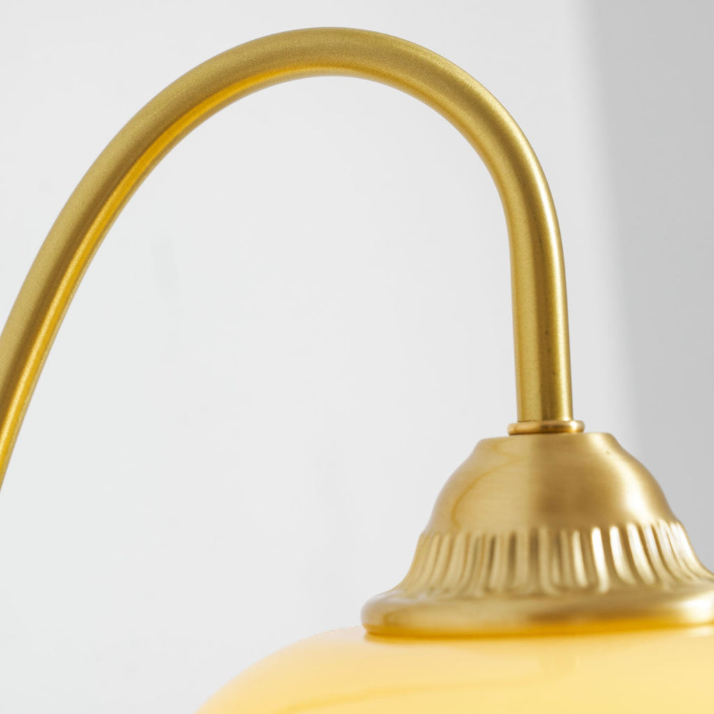 Close view of the curved brass arm and the ridged cap above the glass shade on this Clérachic wall light.