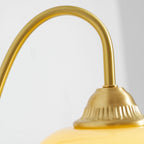 Close view of the curved brass arm and the ridged cap above the glass shade on this Clérachic wall light.