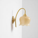 Unlit Clérachic wall light with a cream glass shade on a curved brass arm, near a wall corner.