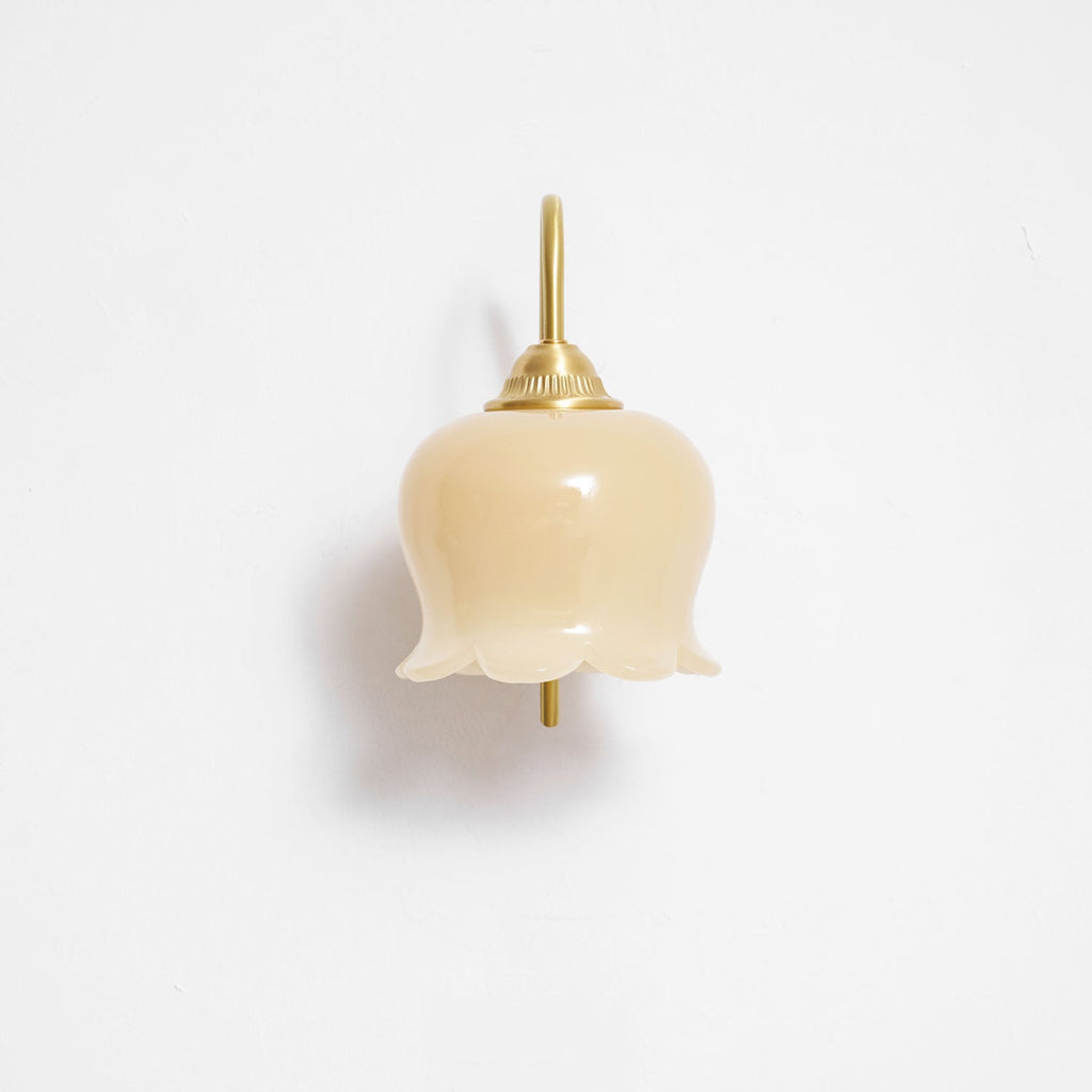 Front view of the unlit Clérachic wall light, its cream glass shade hanging below a brass cap on a white wall.