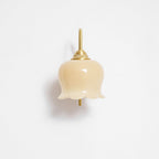 Front view of the unlit Clérachic wall light, its cream glass shade hanging below a brass cap on a white wall.
